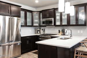 Kitchen featuring high end appliances, glass insert cabinets, a peninsula, decorative light fixtures, and a kitchen breakfast bar