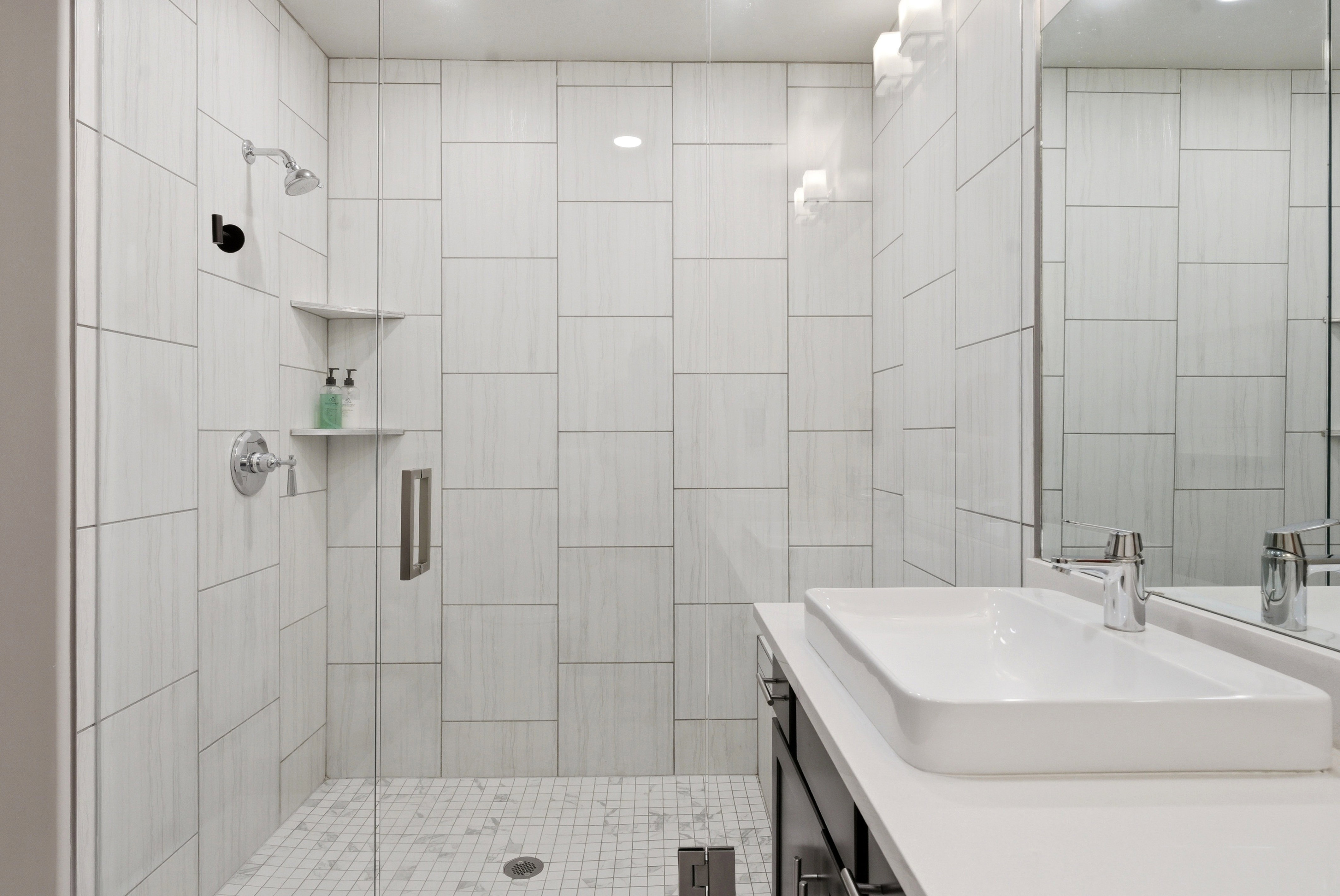 Contemporary bathroom featuring a frameless glass shower enclosure, white subway tile shower surround, and a white rectangular vessel sink with a chrome faucet