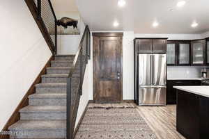 Kitchen featuring glass insert cabinets, high quality fridge, light countertops, light wood-style floors, and dark brown cabinets