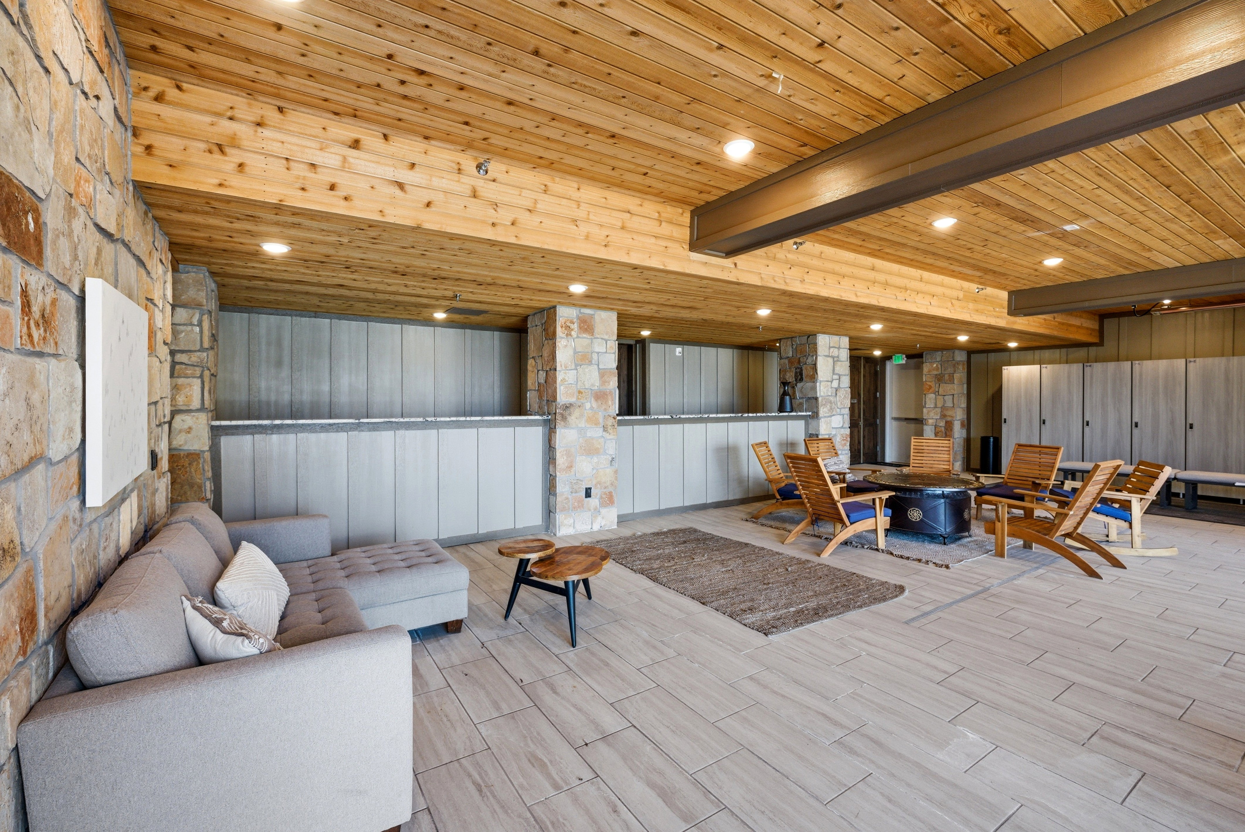 Spacious interior featuring a wood plank ceiling with recessed lighting, exposed structural beams, tile flooring, and stone accent walls