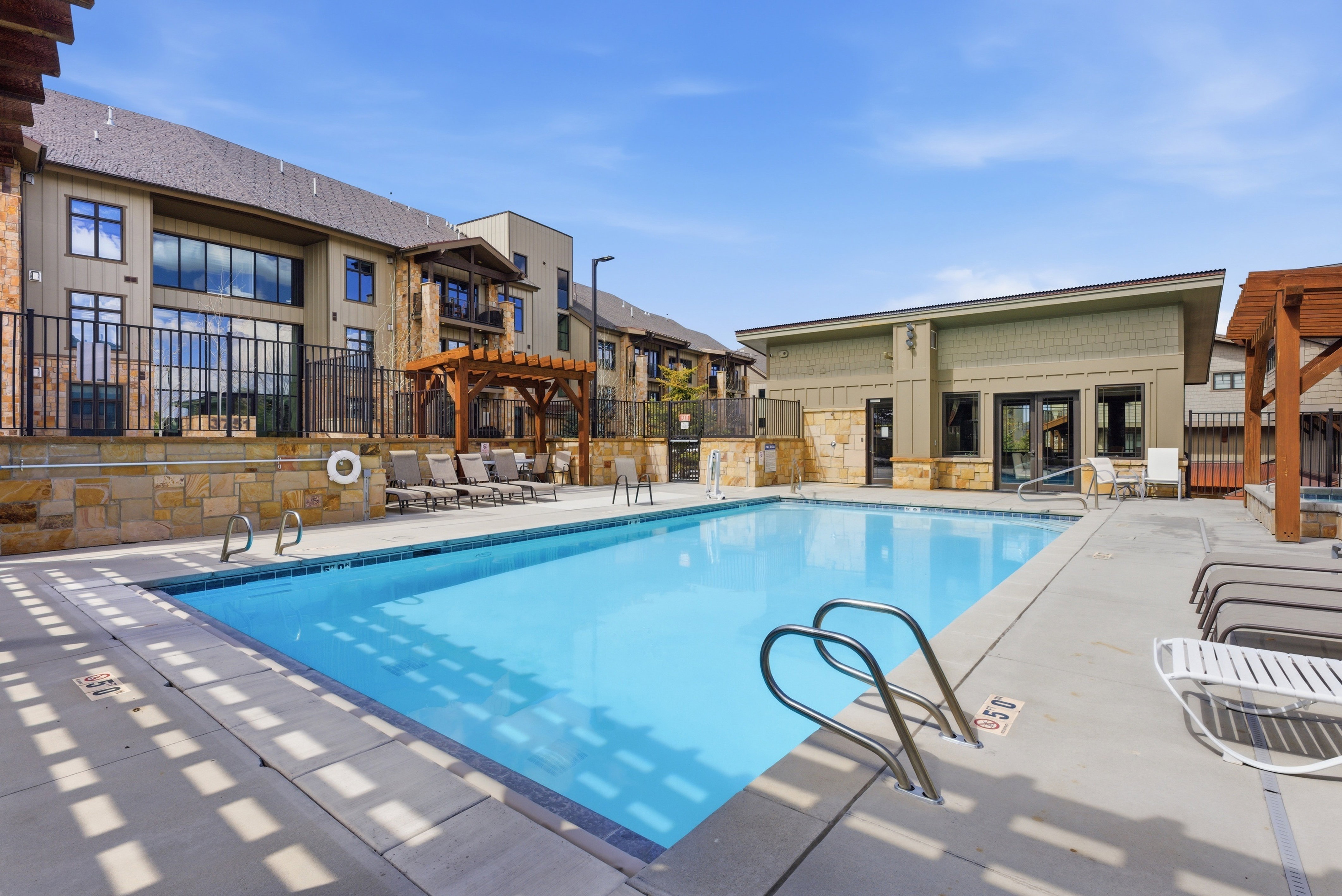 Outdoor swimming pool featuring a perimeter concrete deck, integrated steps, and stainless steel handrails