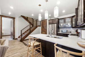 Kitchen featuring a large island with white countertop, dark wood-finish cabinetry, stainless steel refrigerator, and pendant lighting