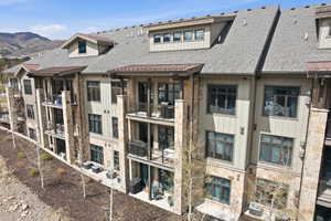 Multi-story building featuring stone and siding exterior, multiple balconies, dark-framed windows, and sloped roofing with dormers