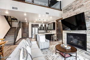 Living area featuring stairs, light wood finished floors, a towering ceiling, a stone fireplace, and recessed lighting