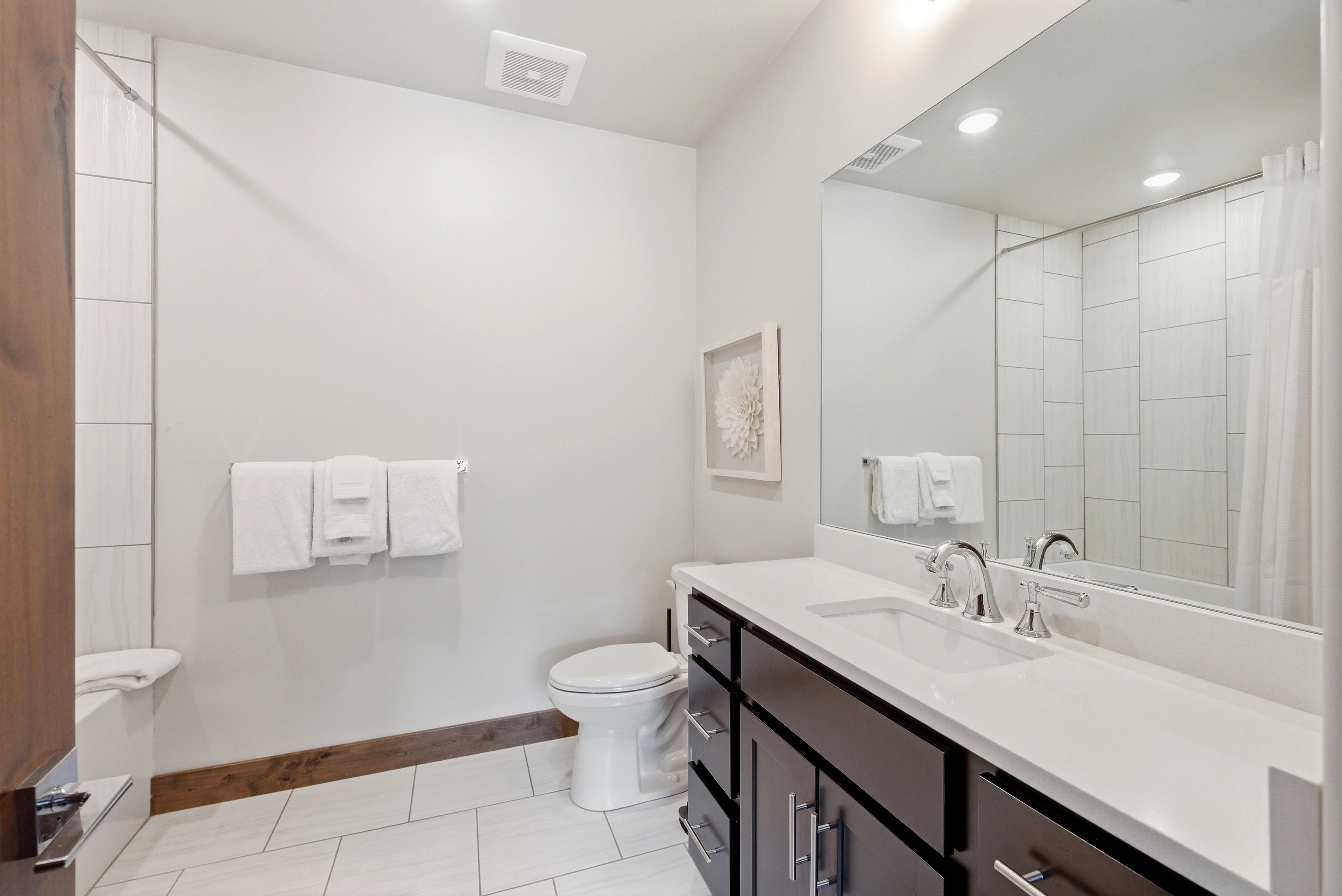 Bathroom featuring a dark wood-finish vanity with a white countertop and integrated sink, chrome faucet, and expansive wall-mounted mirror