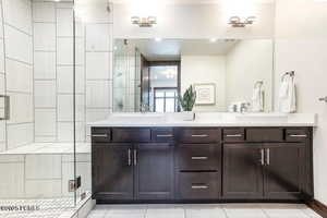 Full bath with double vanity, a stall shower, and light tile patterned flooring