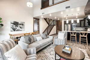 Living room with a high ceiling, stairway, light wood finished floors, and recessed lighting