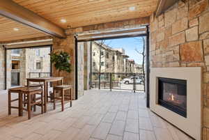 Covered outdoor living space featuring stone walls, a wood-paneled ceiling, and light-colored tile flooring