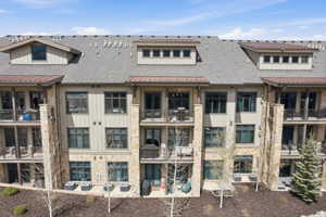 Multi-story condominium building featuring stone and siding exterior, multiple balconies, individual patios, and dormer windows