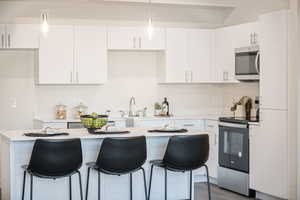 Kitchen featuring appliances with stainless steel finishes, hanging light fixtures, a kitchen breakfast bar, white cabinets, and light wood-type flooring