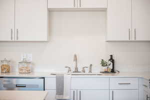 Kitchen featuring light stone countertops, white cabinetry, and stainless steel dishwasher