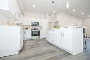 Kitchen featuring white cabinets, appliances with stainless steel finishes, a kitchen island, a kitchen breakfast bar, and light countertops