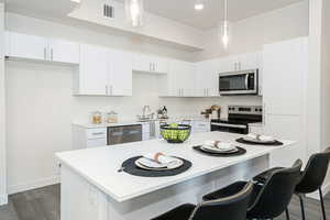 Kitchen featuring appliances with stainless steel finishes, white cabinets, dark wood finished floors, and decorative light fixtures