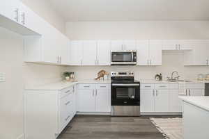 Kitchen featuring stainless steel appliances, white cabinetry, dark wood-style flooring, and light stone counters