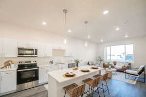 Kitchen featuring stainless steel appliances, white cabinets, pendant lighting, dark wood-style floors, and a kitchen breakfast bar