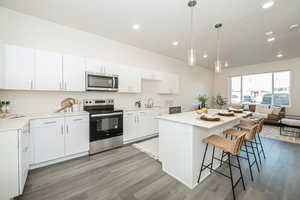 Kitchen with stainless steel appliances, white cabinets, pendant lighting, light wood finished floors, and a kitchen bar
