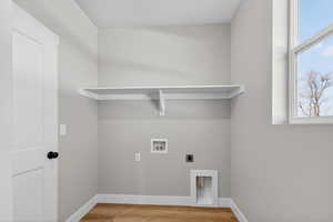 Washroom with electric dryer hookup, hookup for a washing machine, and light wood-type flooring