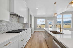 Kitchen with white cabinets, light stone countertops, stainless steel appliances, a chandelier, and light wood-style floors
