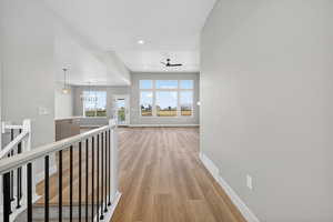 Hall featuring light wood-style floors, a chandelier, recessed lighting, and an upstairs landing