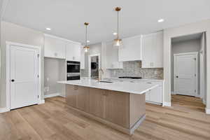 Kitchen featuring decorative light fixtures, white cabinets, a kitchen island with sink, tasteful backsplash, and recessed lighting