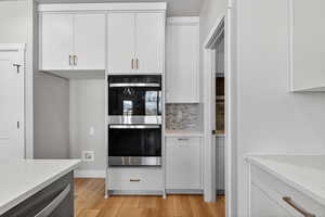 Kitchen with stainless steel appliances, light stone countertops, white cabinets, light wood-style floors, and decorative backsplash