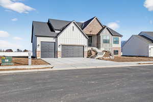 View of front facade with board and batten siding, concrete driveway, an attached garage, roof with shingles, and brick siding