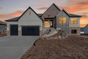 View of front facade with concrete driveway, board and batten siding, an attached garage, and brick siding