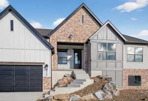 View of front of property featuring board and batten siding, brick siding, an attached garage, and driveway