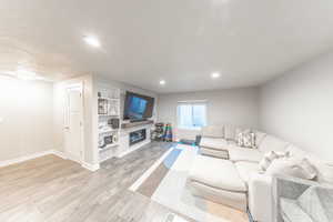 Living room featuring built in shelves, light wood-style flooring, a glass covered fireplace, recessed lighting, and a textured ceiling