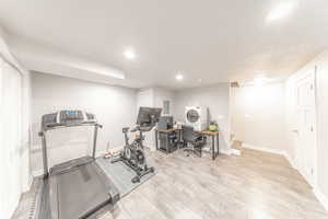 Exercise area with recessed lighting, light wood-style floors, and electric panel