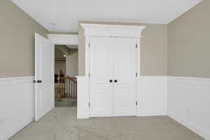 Unfurnished bedroom with a wainscoted wall, light carpet, and a closet
