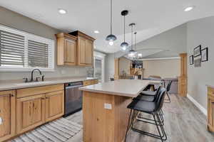 Kitchen featuring open floor plan, a kitchen island, a kitchen bar, stainless steel dishwasher, and vaulted ceiling
