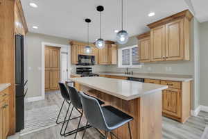 Kitchen featuring a breakfast bar area, pendant lighting, black appliances, a kitchen island, and recessed lighting