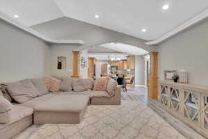 Living area featuring arched walkways, decorative columns, a chandelier, light wood-style floors, and recessed lighting