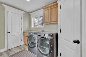 Laundry area with cabinet space, light wood finished floors, and washing machine and dryer