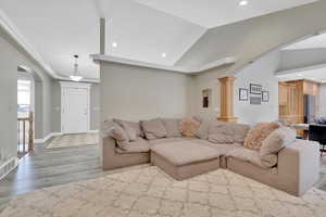 Living area featuring arched walkways, recessed lighting, light wood-style floors, and vaulted ceiling