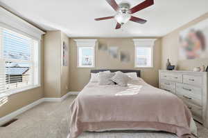 Bedroom with light colored carpet, ceiling fan, and multiple windows
