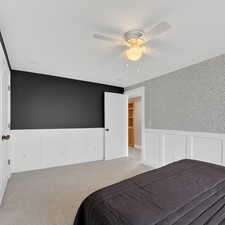 Bedroom with a wainscoted wall, a decorative wall, carpet floors, and a ceiling fan