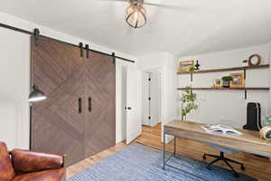 Office featuring light wood-style floors, a textured ceiling, and a barn door