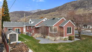 Back of house featuring a storage shed, brick siding, a mountain view, a shingled roof, and a yard