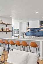 Kitchen with open shelves, a kitchen bar, light wood-style floors, white cabinetry, and light stone countertops