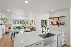 Kitchen with light stone counters, white cabinets, light wood-type flooring, a peninsula, and dishwasher