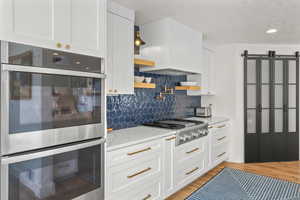 Kitchen featuring stainless steel appliances, white cabinets, light stone countertops, backsplash, and light wood-type flooring