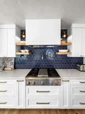 Kitchen with open shelves, white cabinets, stainless steel gas cooktop, light stone counters, and a textured ceiling
