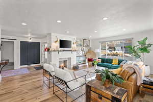 Living area featuring light wood-style floors, a warm lit fireplace, and recessed lighting