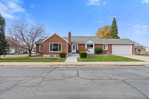View of front facade with brick siding, a front yard, concrete driveway, a chimney, and a garage