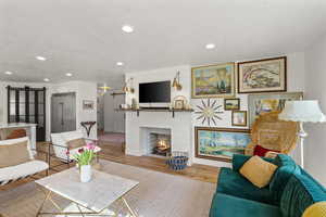 Living area featuring a barn door, wood finished floors, a large fireplace, and recessed lighting