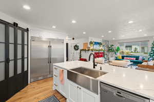 Kitchen with white cabinetry, appliances with stainless steel finishes, light stone counters, light wood-type flooring, and open floor plan