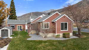 View of front of property with a mountain view, a storage shed, brick siding, and a front yard
