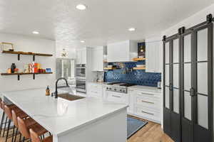 Kitchen with open shelves, light stone counters, white cabinets, a kitchen bar, and a peninsula